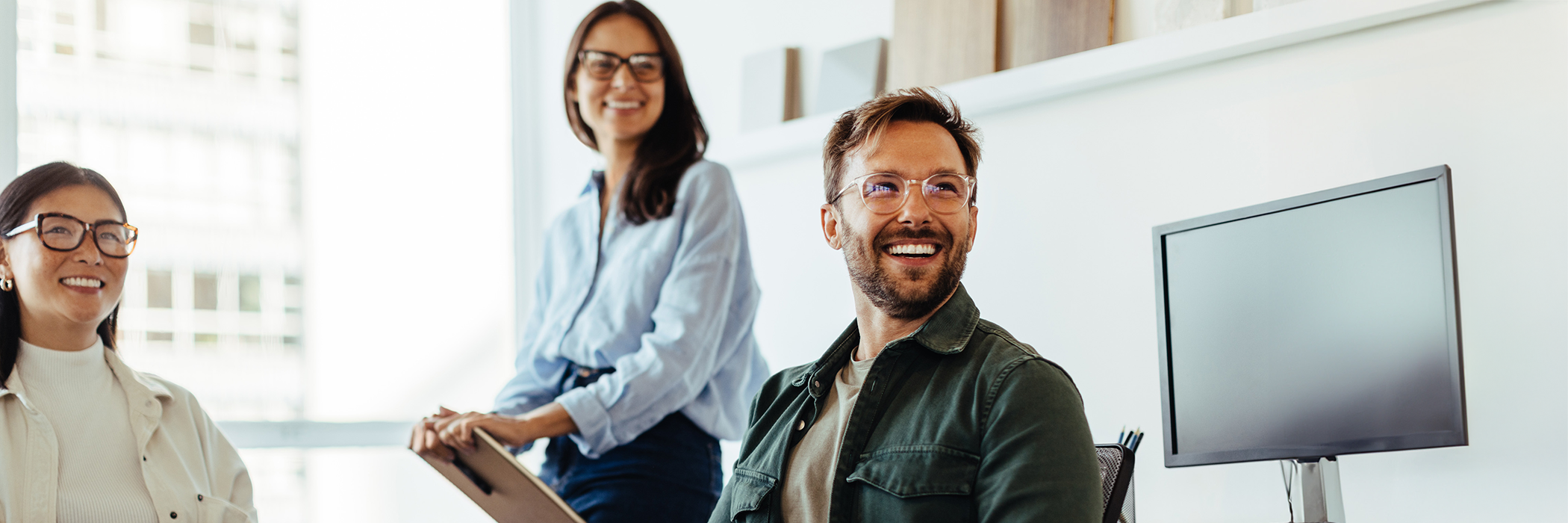 Drei Personen sitzen lächelnd zusammen in einem Büro