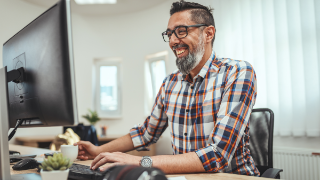 A successful smiling freelance man is working on a new project in the office. He is looking at project on a computer.