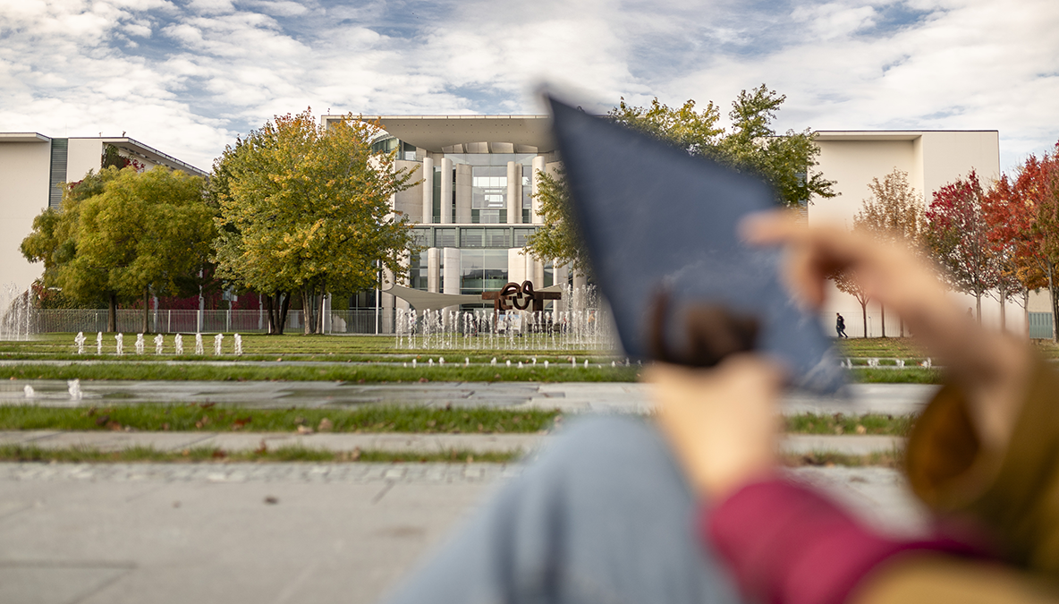 DPS, News: Paper Big Data in Policy Making Gebäude des Bundes Kanzleramts in Berlin, im Vordergrund unscharf eine Person mit Tablet