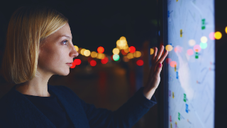 Young female tourist using smart city gadget to get direction in Barcelona central, female in night city standing front big digital screen with city map routes and locations shown on it,filtered image