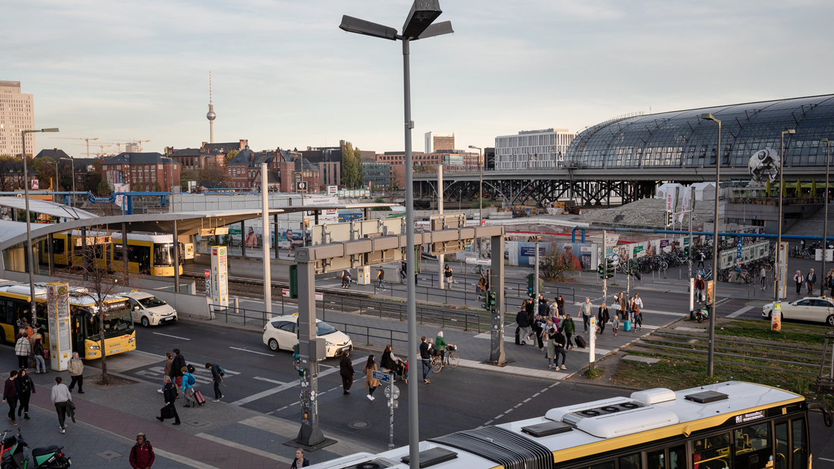 DPS, Projekt, Vorschaubild: Urbanite Busbahnhof am Berliner Hauptbahnhof mit dem Hauptbahnhof und Fernsehturm im Hintergrund, Menschen überqueren Fußgängerampel