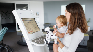 Eine Mutter steht mit ihrem Kind vor einem Terminal zur Beantragung von Kindergeld.