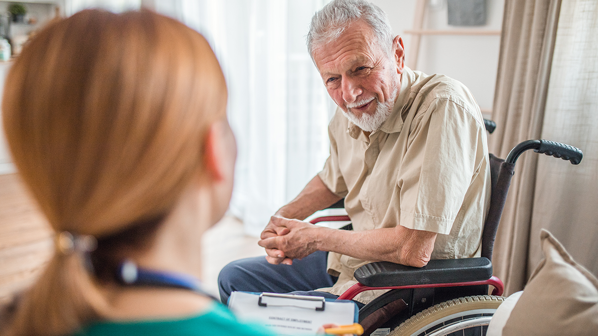 Senior man in a wheelchair receives medical support and health care from a nurse at home. Caregiver, and seniors with disabilities, patient ready for physiotherapy