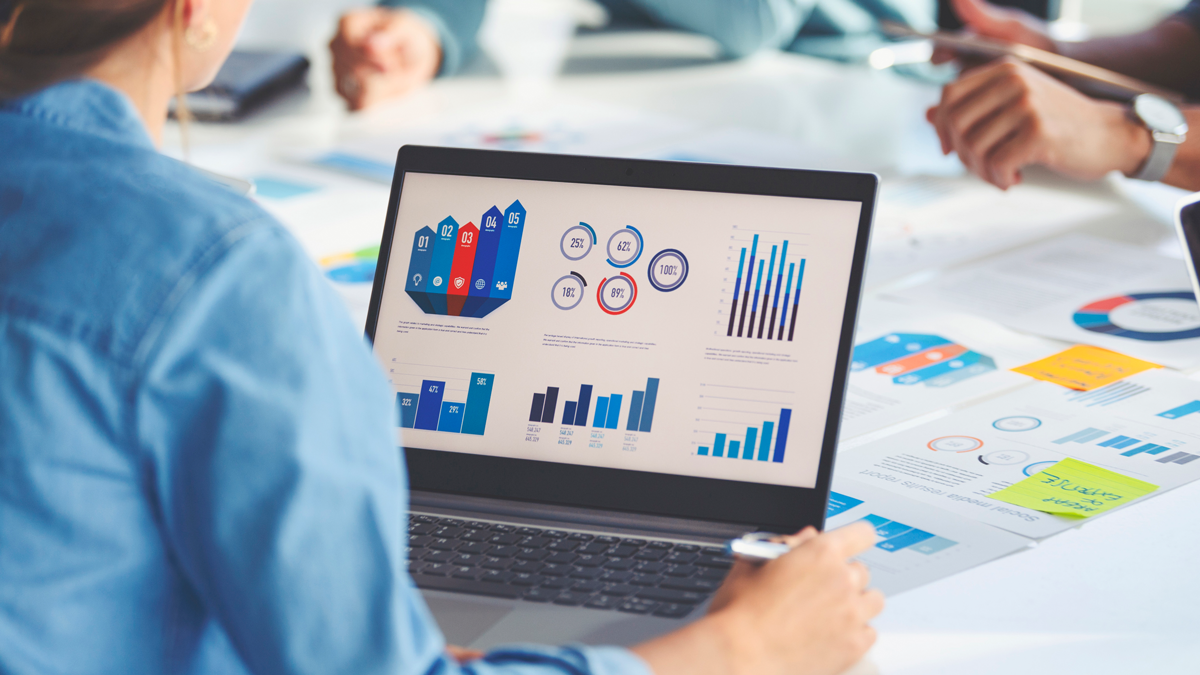 Multi racial group of people working with Paperwork on a board room table at a business presentation or seminar. The documents have financial or marketing figures, graphs and charts on them. There is a laptop with graph and chart data