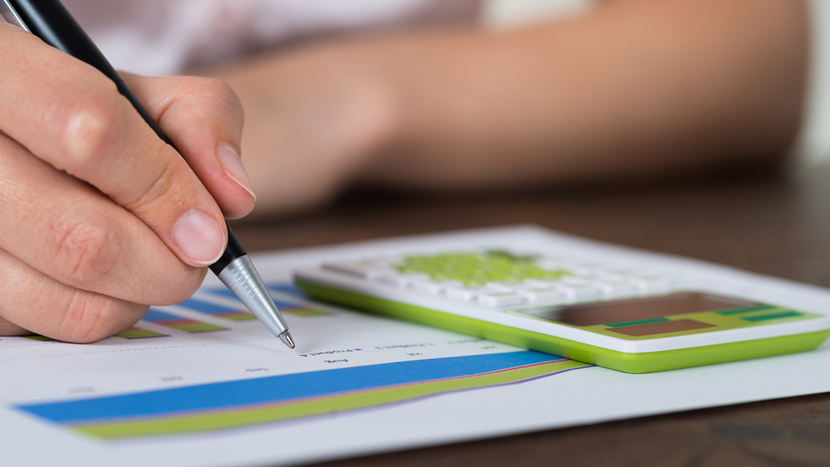 Close-up Of Businesswoman Analyzing Graph With Calculator At Desk