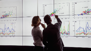 Business men in a dark room standing in front of a large data display