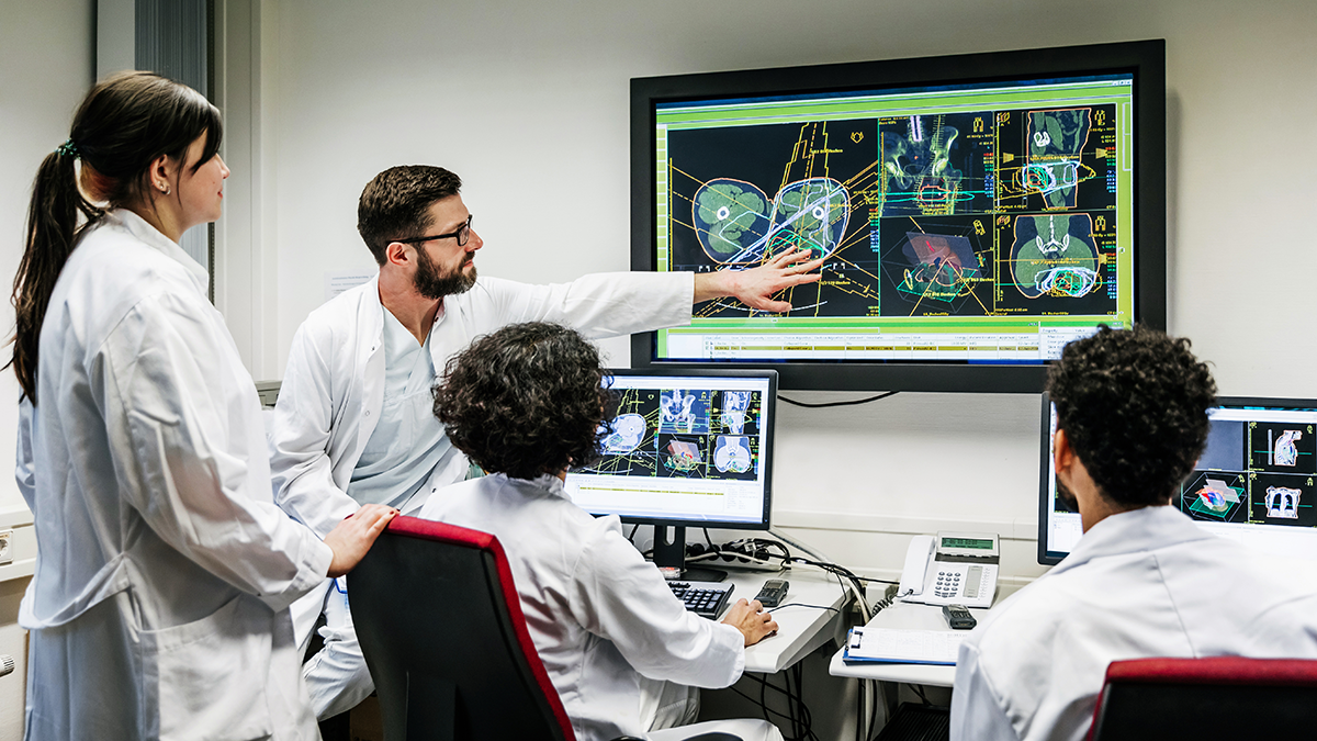 A group of clinical doctors discussing a patient's test results on a large monitor in an office.