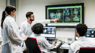 A group of clinical doctors discussing a patient's test results on a large monitor in an office.