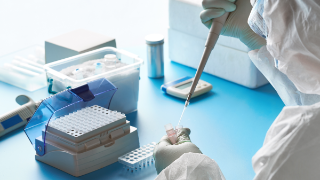 Forscher in Schutzanzug, Maske und Brille arbeitet mit Patientenabstrichen