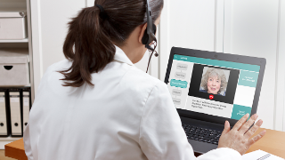 Frau in weißem Kittel spricht in einer Videokonferenz im digitalen Therapieprogramm DysarTrain mit einer Seniorin