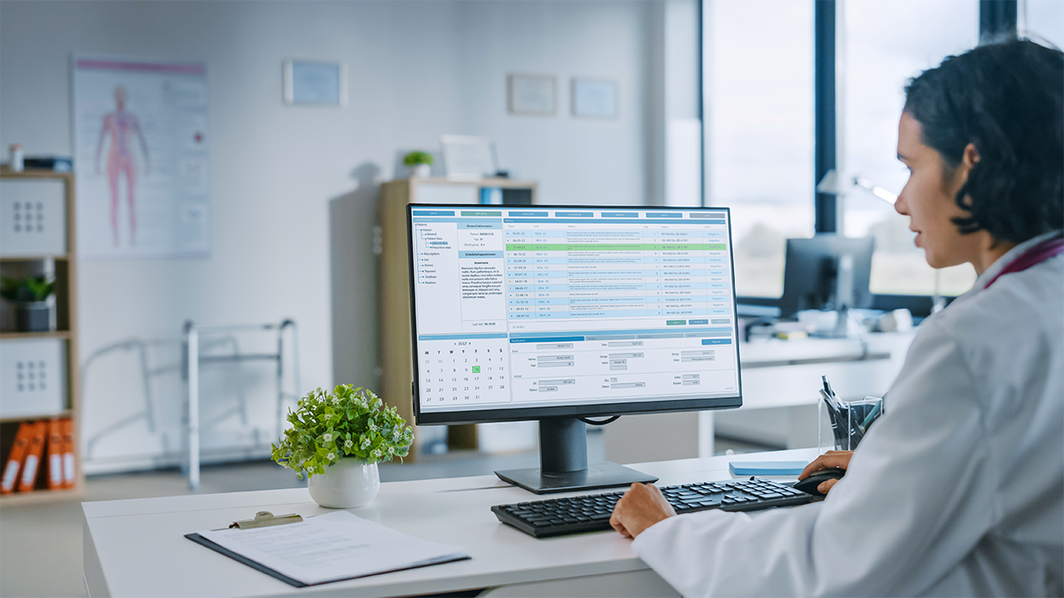 Experienced Female Medical Doctor Wearing White Coat Working on Personal Computer in a Health Clinic. Medical Health Care Professional Working with Test Results, Patient Treatment Planning.