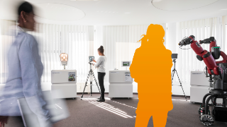 Einladung zum Netzwerktreffen "Werde eine von uns!": IioT-Lab am Fraunhofer FOKUS, in dem 2 Frauen arbeiten und der Umriss einer Person in Orange eingefügt wurde