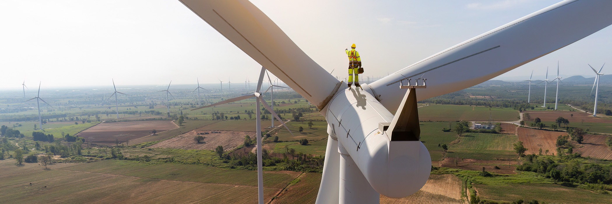 Engineer wearing uniform holding equipment box standing[ on windmill under work inspection and checking survey. Windmill turbine farm rotation to electricity energy.
