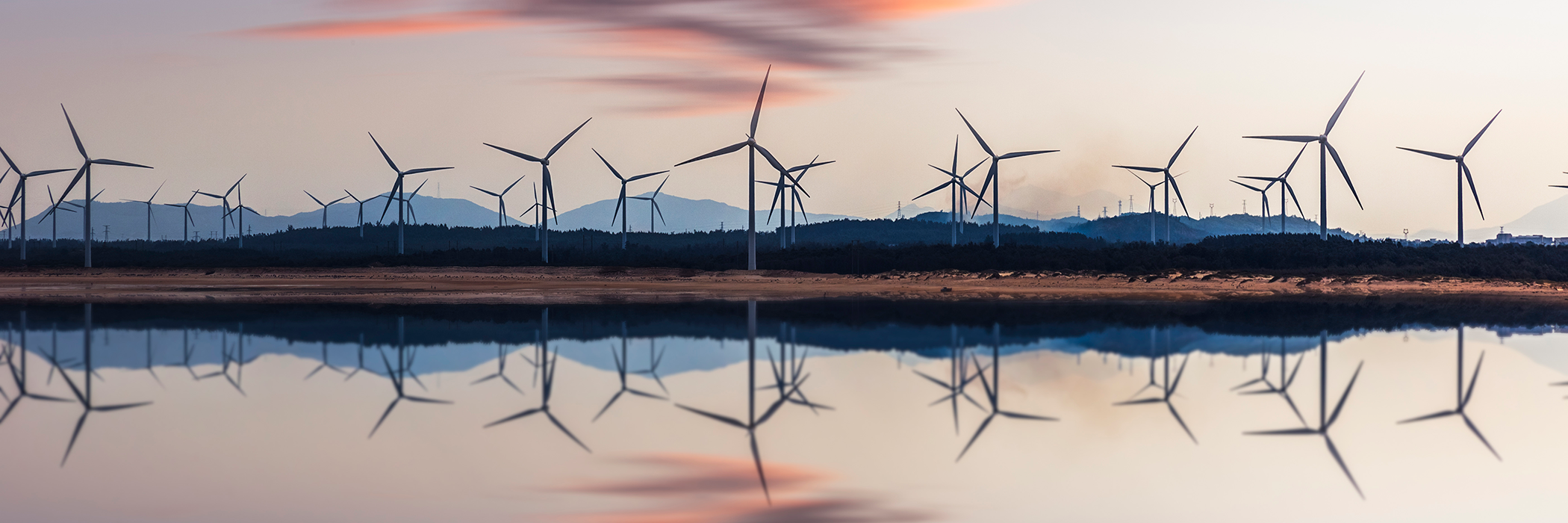 Eine Reihe Windräder spiegelt sich in einer Wasseroberfläche, Abendstimmung