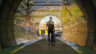 Siluette einer Person hinter einer Glastür, die zu einem mit LED-Wänden beleuchteten Tunnel führt
