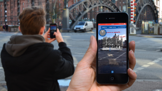 Passanten nutzen AR-Anwendung auf dem Smartphone, um Informationen über die Brooksbrücke in Hamburg via App aus dem Projekt Speicherstadt Digital zu erhalten