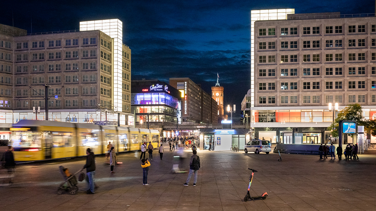 Blick vom Berliner Alexanderplatz Richtung Rotes Rathaus mit beleuchteten Schaufenstern, Menschen und einer fahrenden Straßenbahn
