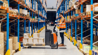 A forklift driver is driving modern sustainable vehicle and collecting boxes with goods in import and export firm.