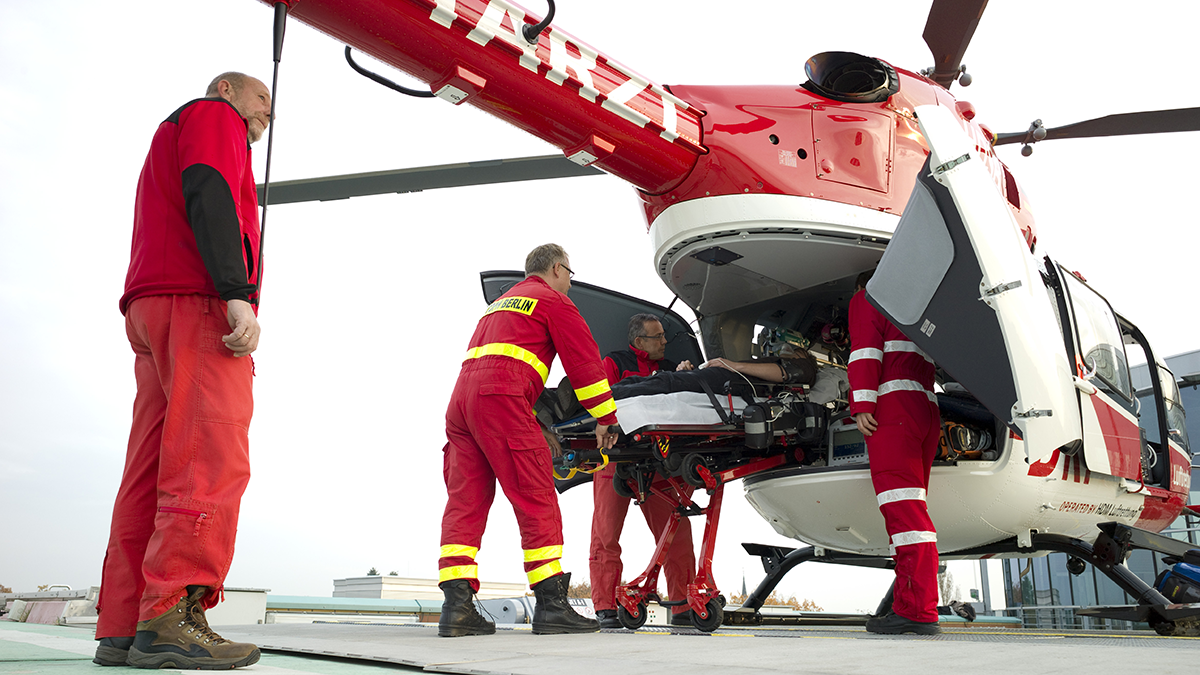 Rettungshubschrauber auf dem Dach des Unfallkrankenhaus Marzahn in 4 Sanitäter einen Patienten auf einer Trage verladen
