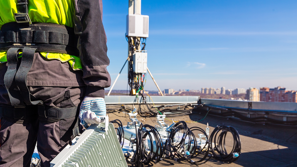 Person in Arbeitskleidung auf einem Dach trägt ein Bauteil zu einer Mobilfunkantenne