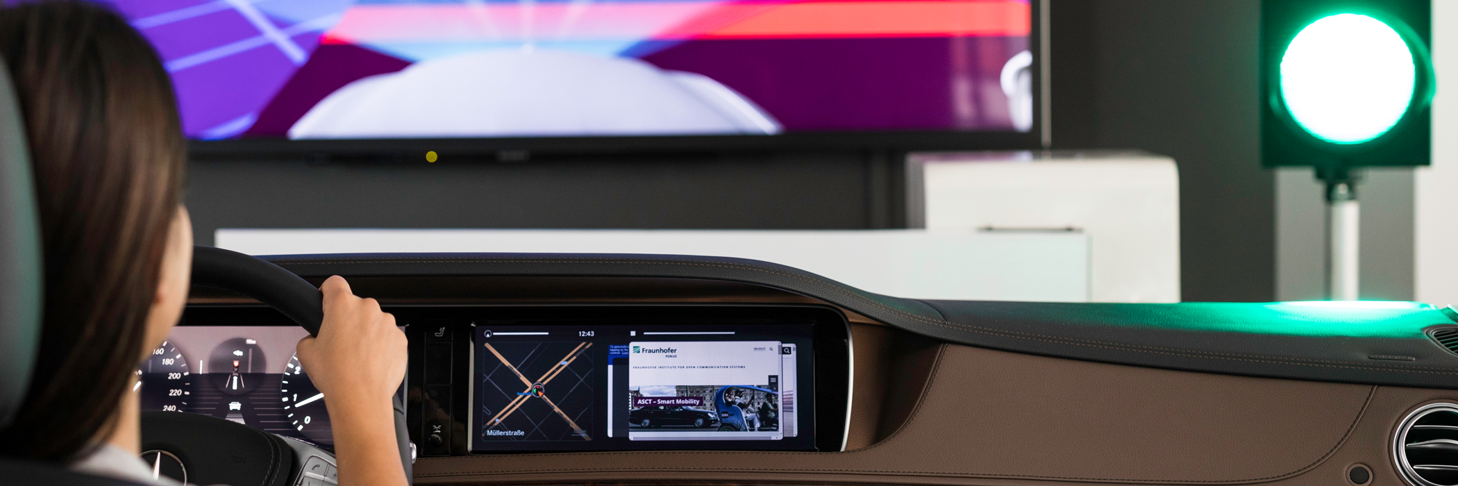 Eine Frau sitzt am Steuer eines Fahrzeugsimulators im Smart Mobility Lab von Fraunhofer FOKUS, vor ihr eine grüne Ampel.