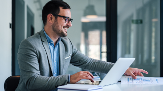 Delighted bearded, adult man wearing glasses, making sure his office desk is tidy.