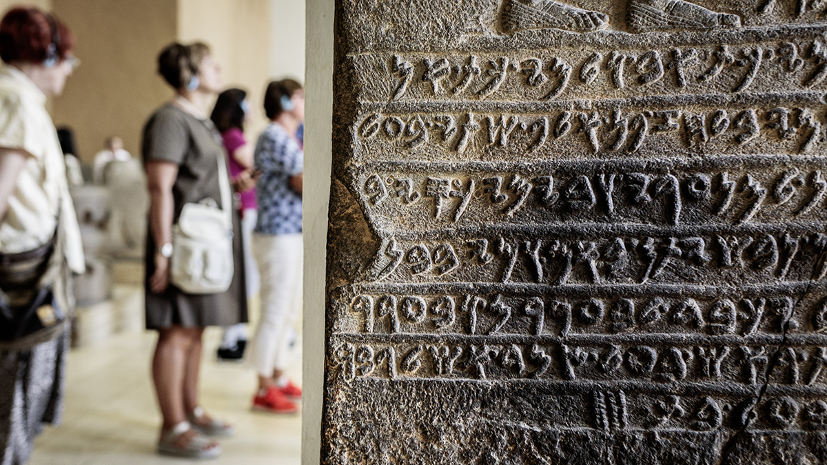 DPS, Projekte: Base4NFDI Steintafel mit Schriftzeichen in einem Museum, im Hintergrund Besucherinnen mit Kopfhörern