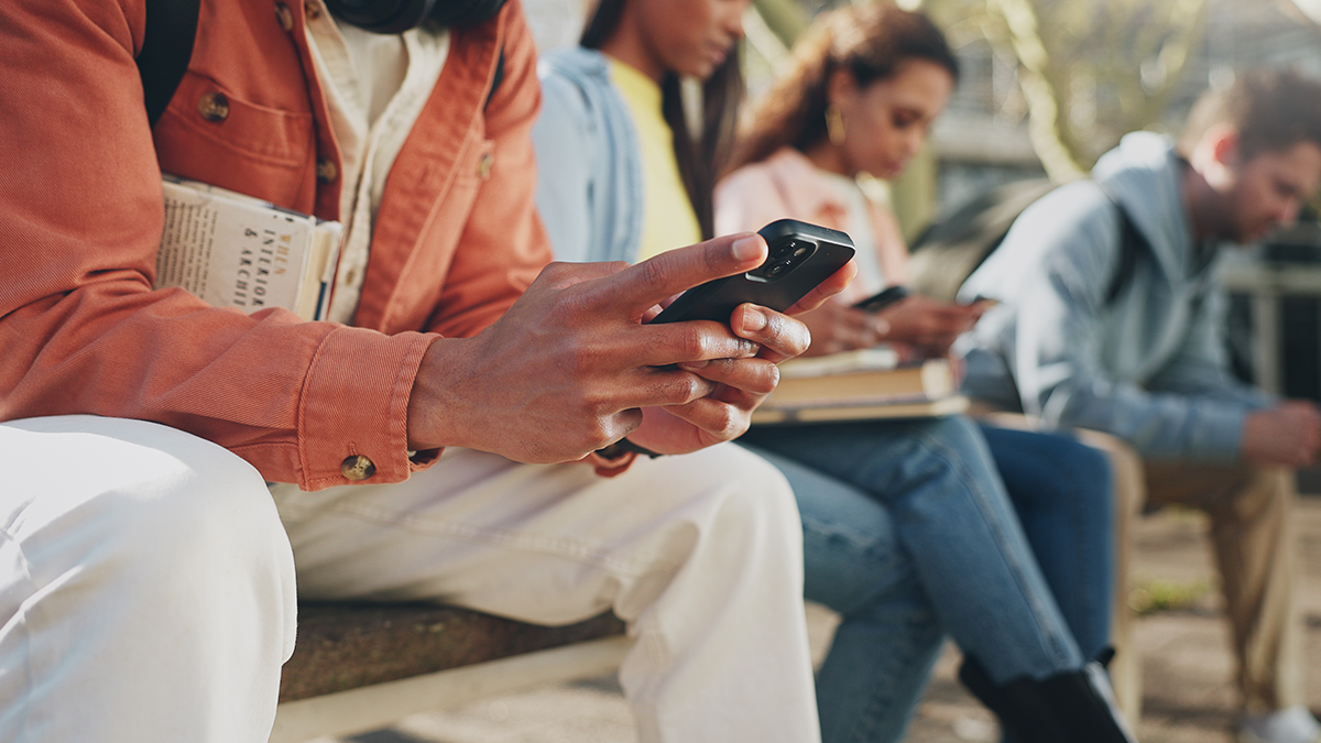 Diverse Gruppe von Personen sitzt mit Büchern und Smartphones auf einer Parkbank
