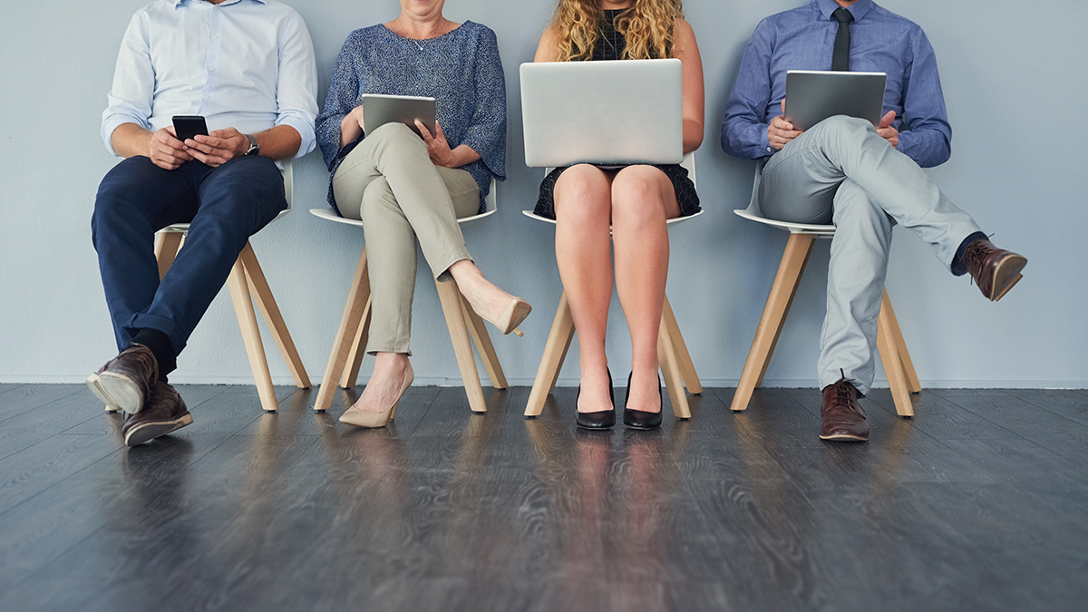 Studio shot of a group of unrecognizable businesspeople using their wireless devices while being seated against a grey background
