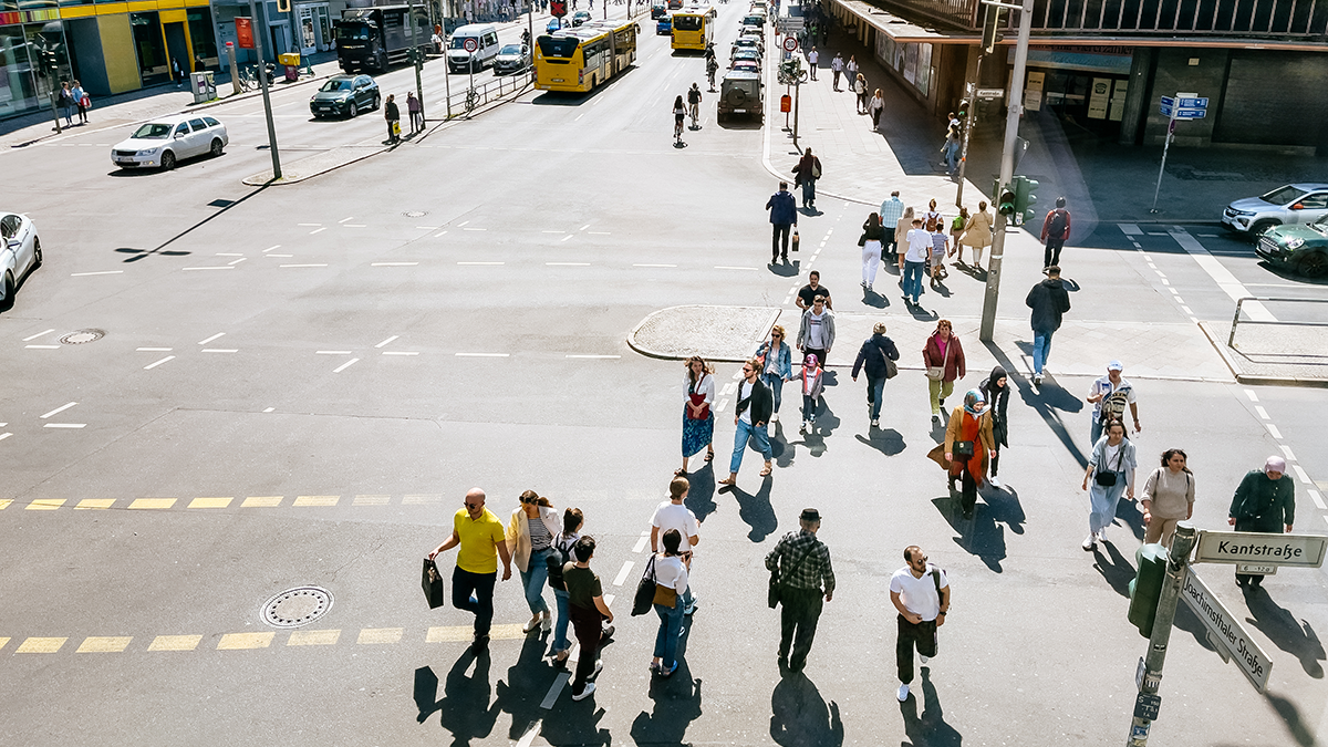 ESPRI, Projekt, Vorschaubild: OPTI-ALERT View from above of a busy street in Berlin's Mitte district. A large group of people are crossing the street on a green light, while cars and public transportation move along the wide street. Office buildings and various shops line the left and right sides of the street.