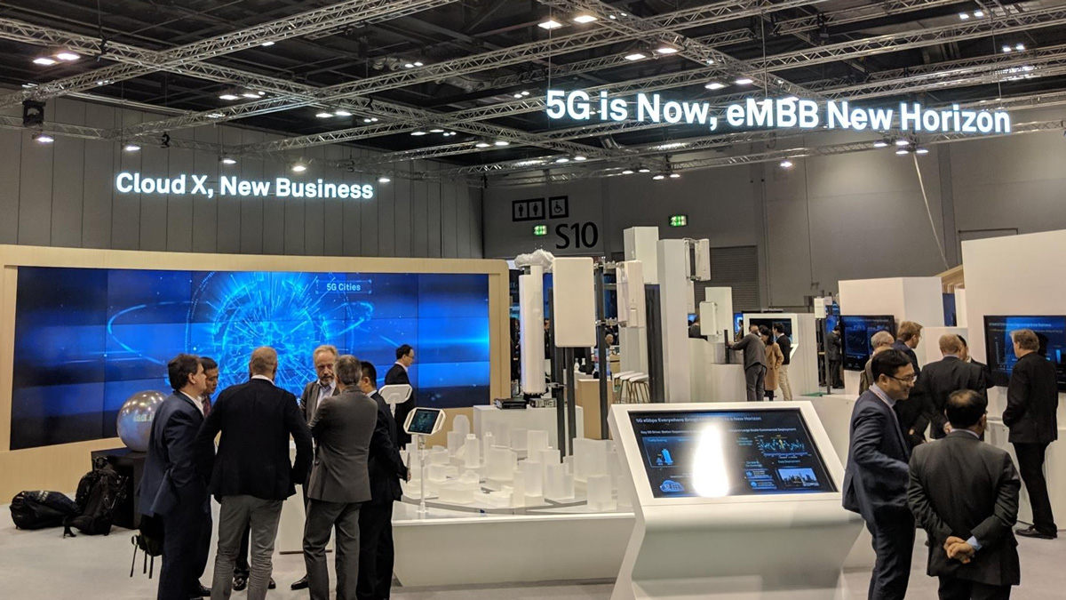 Global eMBB Forum 2018: Messehalle mit Bildschirmen und Ausstellungsstücken neben denen Besucher stehen.