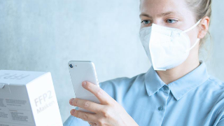 FAME, News: smartID Eine Frau mit FFP2-maske macht ein Foto von einer Verpackung mit ihrem Smartphone.