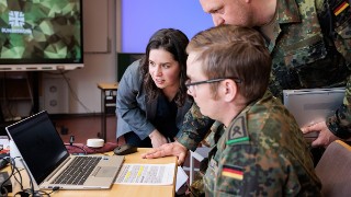 Mitarbeitende der Bundeswehr arbeiten gemeinsam in einer virtuellen Lernumgebung an einem Laptop
