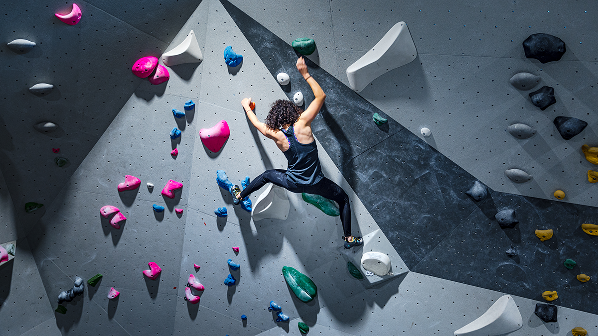 Fit young woman climbing wall in gym. Sportswoman during intense climbing session in an indoor climbing centre.