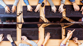 Top view of female students learning computer programming. Girls in computer lab coding on laptops.