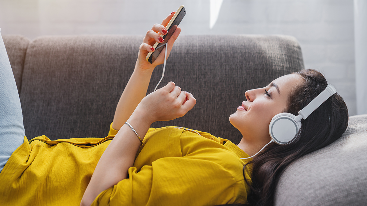 Side view of young woman listening to music online on smartphone in headphones