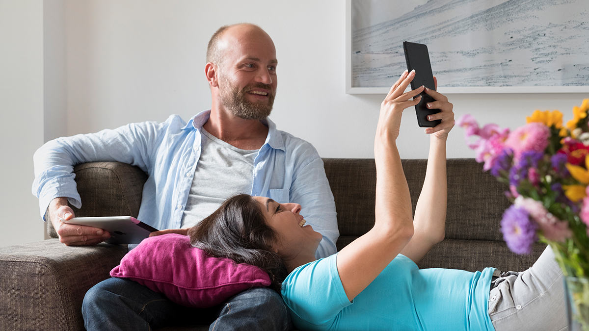 FAME, Projekte: Share It Paar im Wohnzimmer auf dem Sofa, das sich gegenseitig Inhalte auf Tablets zeigt