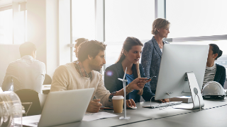 Büro mit einer diversen Gruppe von Personen, Gegenlicht, zwei Personen arbeiten zusammen an einem Bildschirm im Vordergrund