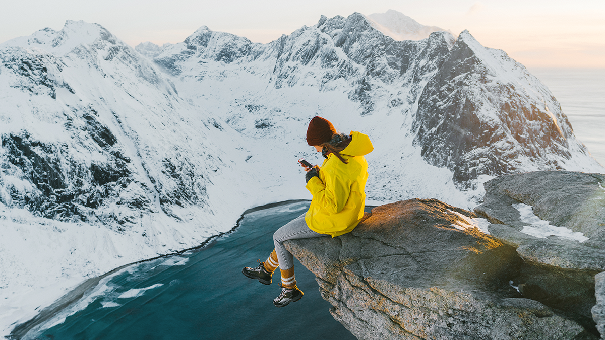 FAME, Projekte: UST+ Home Young Caucasian woman sitting on cliff and using smartphone on Lofoten island in snow