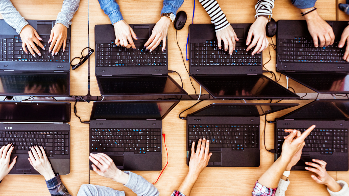 Top view of female students learning computer programming. Girls in computer lab coding on laptops.