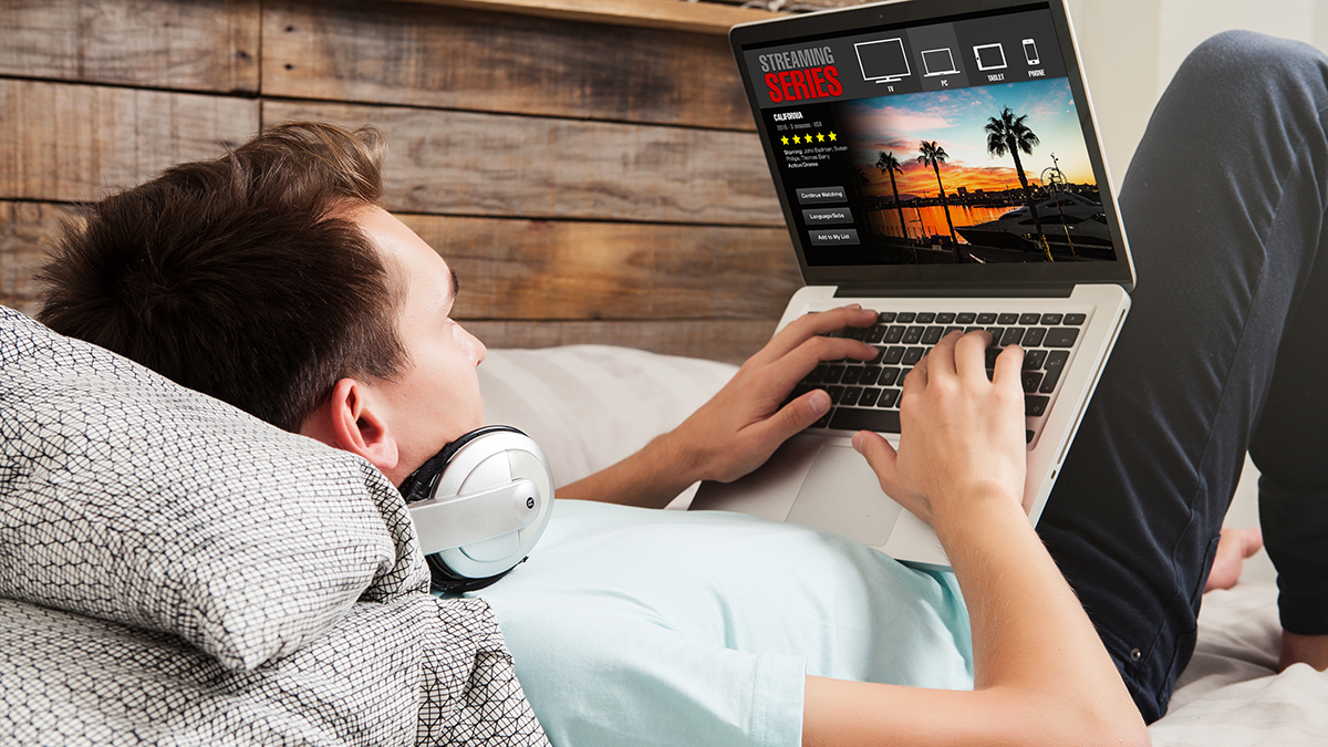 Man watching streaming series in a laptop computer, lying in the bed.