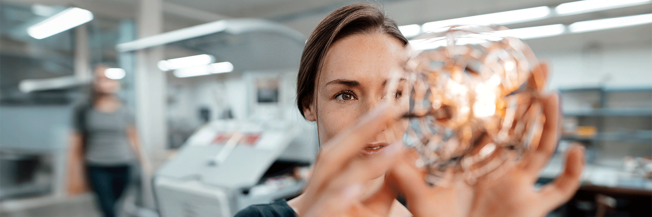 Frau in Laborumgebung betrachtet eine Glühbirne
