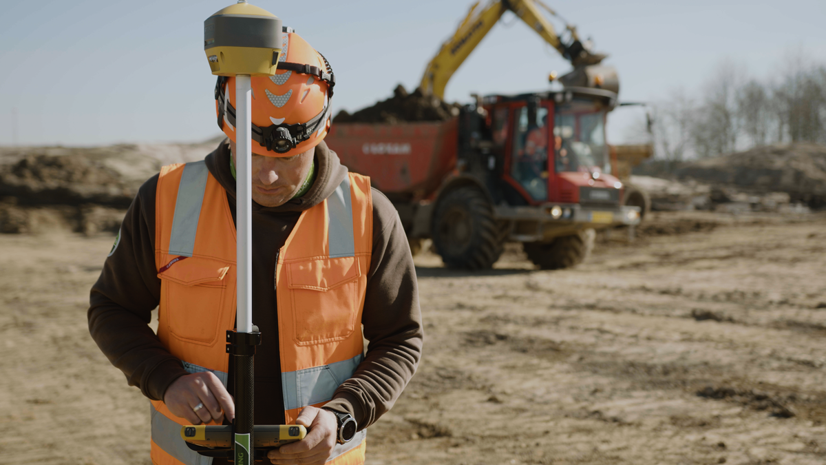 NGNI, Projekt, Vorschaubild: CampusOS Baustelle: Bauarbeiter mit Vermessungsgerät, im Hintergrund ein Bagger und Transporter mit Erde