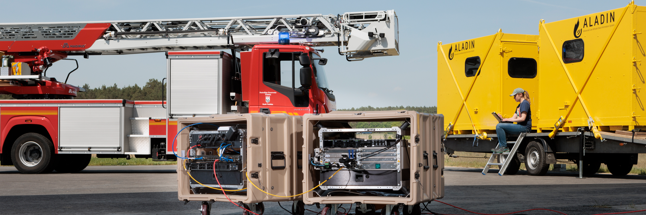 The Fraunhofer FOKUS 5G+ Nomadic Node in 2 portable Boxes in front of a fire truck and two yellow communication containers for the ALADIN project at airfield Schönhagen, Brandenburg, Germany