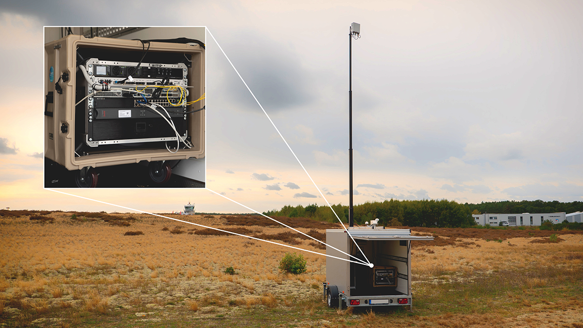 Transportanhänger auf dem Flugfeld Schönhagen mit einer 5G Antenne, vergrößert im Anhänger die Box mit dem Nomadic Node von Frauhofer FOKUS