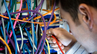 Mitarbeiter in einem Rechenzentrum verbindet Server mit vielen verschiedenfarbigen Kabeln