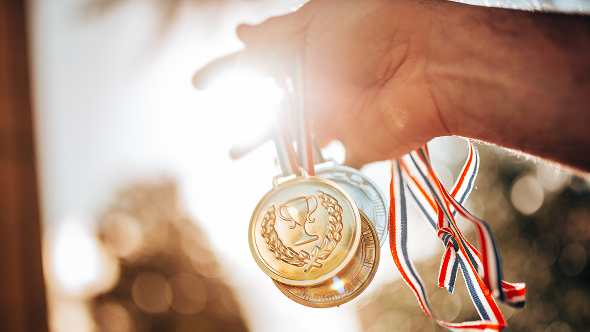 SQC, News: Distinguished Paper Award Eine Hand hält Medaillen für die Sieger:innen
