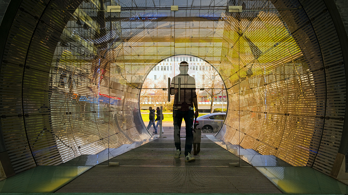 SQC, DANA, Projekte: KI-Energieforum Vorschaubild Siluette einer Person hinter einer Glastür, die zu einem mit LED-Wänden beleuchteten Tunnel führt