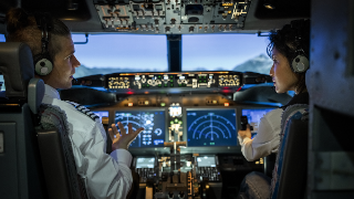 Rear view of a male pilot giving advice to female co-pilot while flying a modern jet airplane. Two pilots sitting in the cockpit and discussing route while flying an commercial airplane jet.