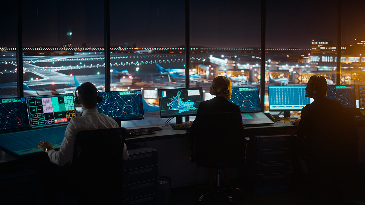Diverse Air Traffic Control Team Working in Modern Airport Tower at Night. Office Room Full of Desktop Computer Displays with Navigation Screens, Airplane Departure and Arrival Data for Controllers.
